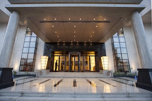 Fachada imponente de un hotel, con grandes puertas de cristal y un interior bien iluminado.
