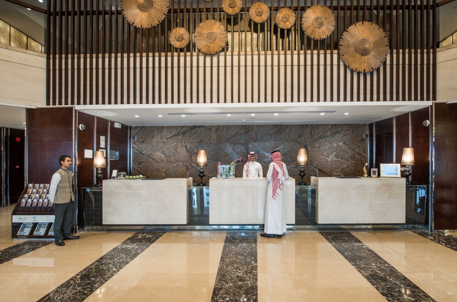 A hotel reception area with a marble floor, two reception desks, and a large wall with a marble pattern.