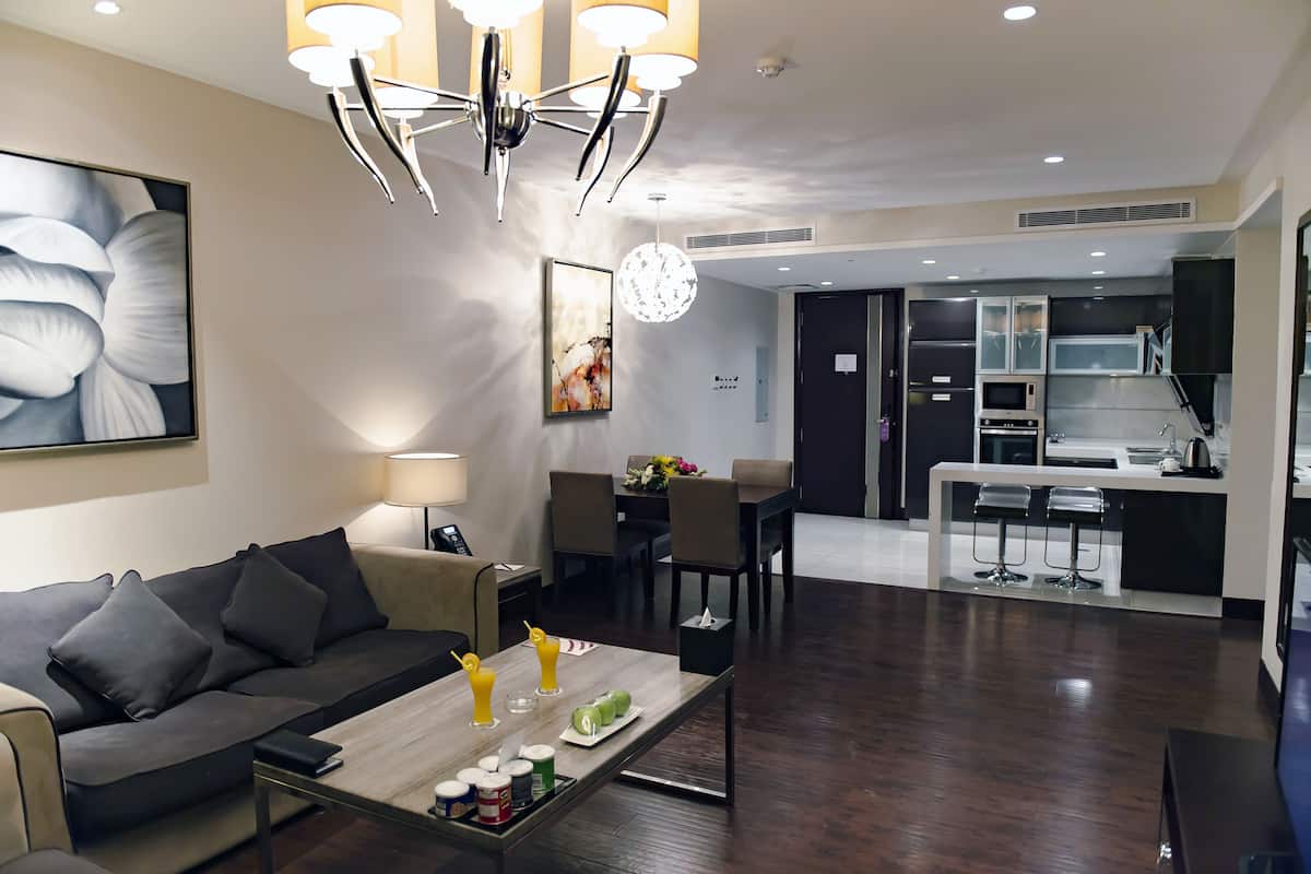 A modern living room with a sofa, coffee table, and a dining area with a table and chairs. There is a kitchen area with a microwave and a sink visible.