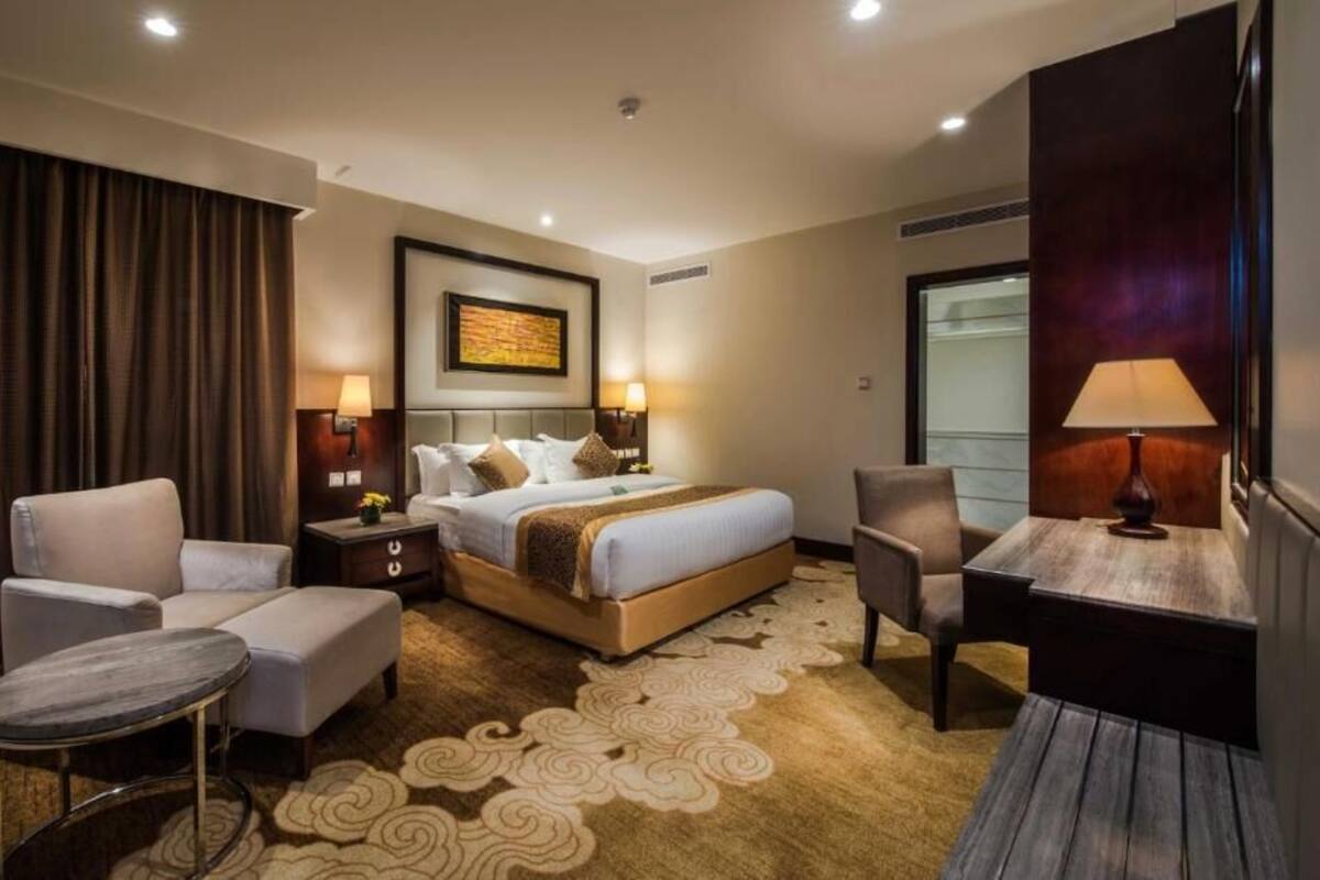 A hotel room with a bed, two armchairs, a small table, and a desk.