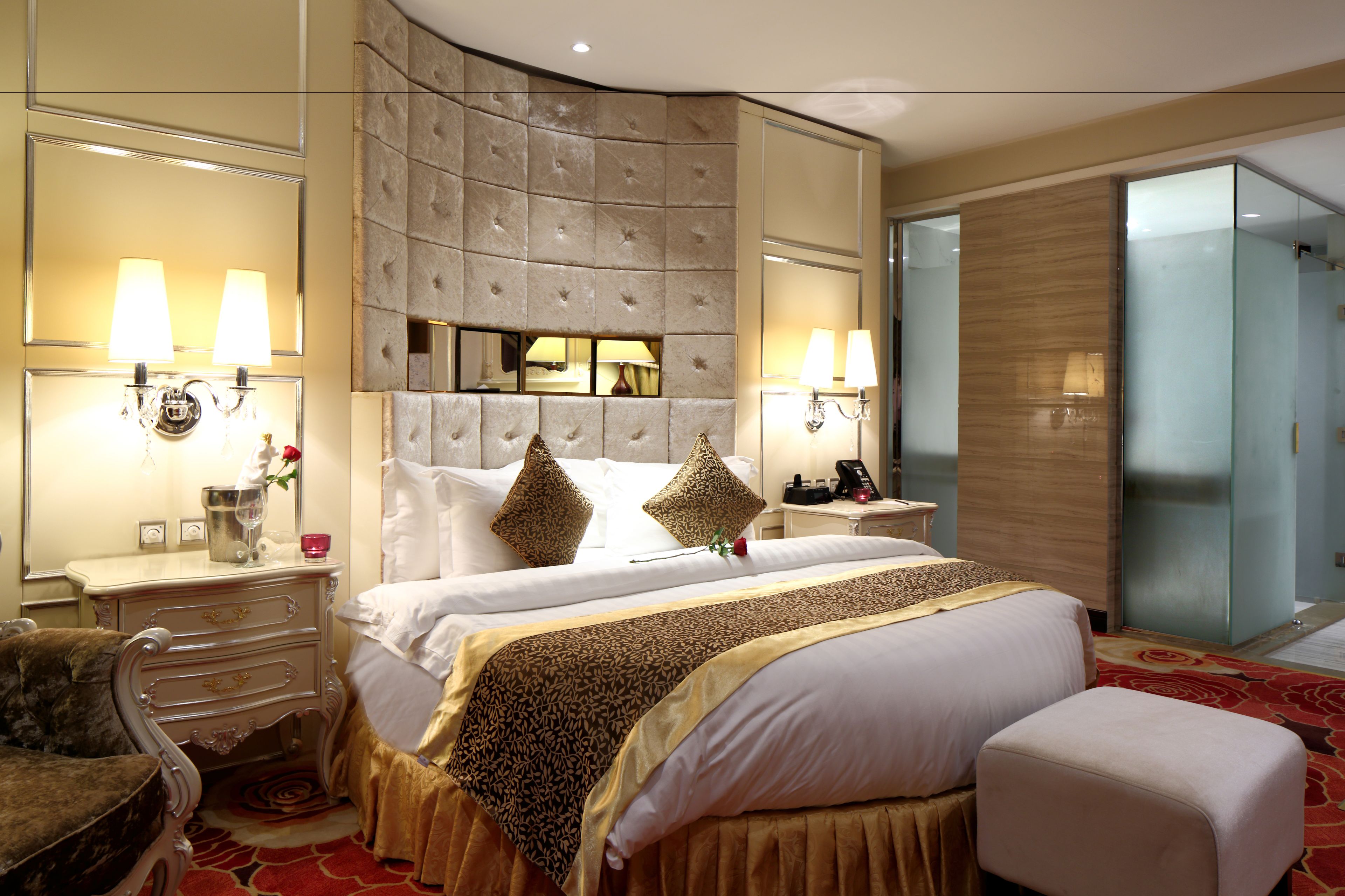 Una habitación de hotel con una cama grande, un cabecero capitonado, dos mesitas de noche con lámparas, un aparador y un espejo.