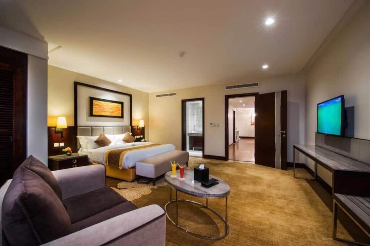 A hotel room with a bed, a sofa, a TV, and a desk with a lamp.