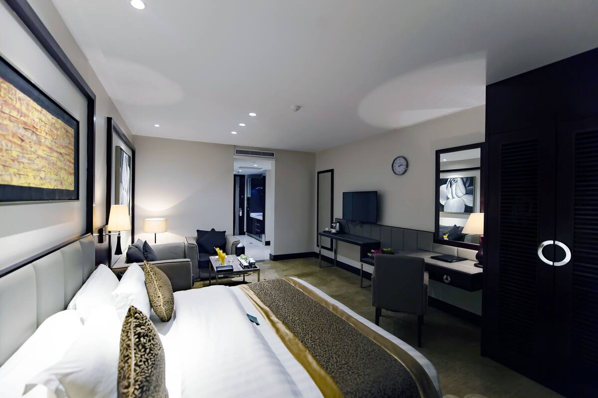 A hotel room with a bed, bedside table, lamp, desk, chair, and a TV.