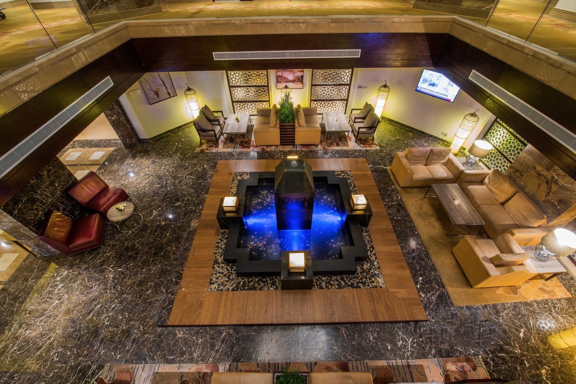 A spacious lobby with a central water feature, seating areas, and a television screen.