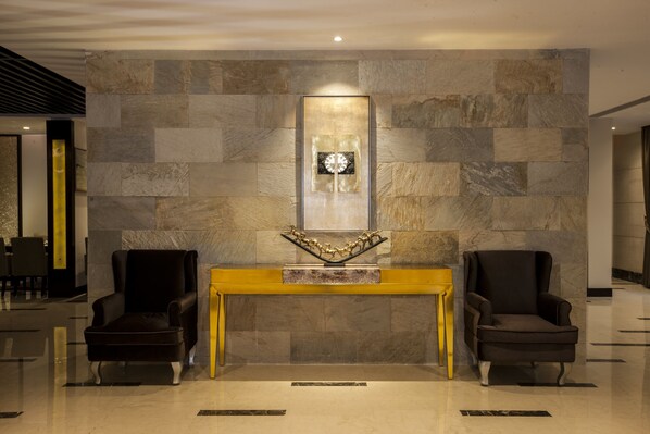 Un hall con pared de piedra, dos sillones, una consola central y una obra de arte enmarcada.