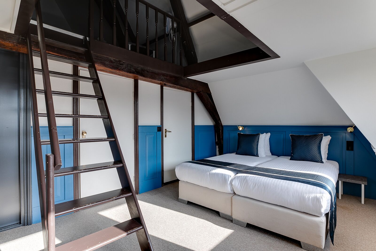 A bedroom with a loft-style ceiling, a bed with white bedding and blue accents, a wooden ladder, and a blue accent wall.
