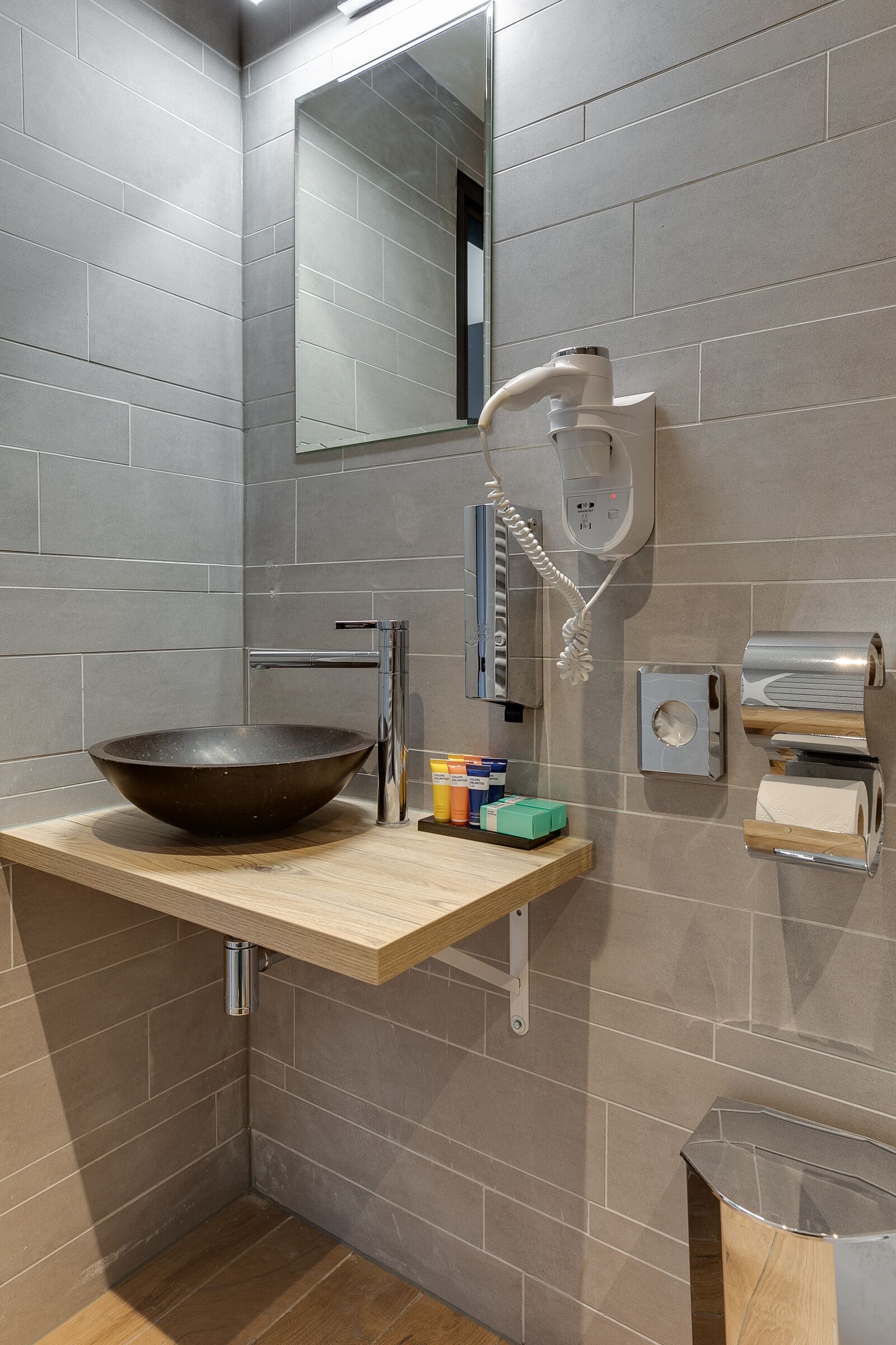 Een moderne badkamer met een grote wastafel, een spiegel, een haardroger en een handdoekdispenser.
