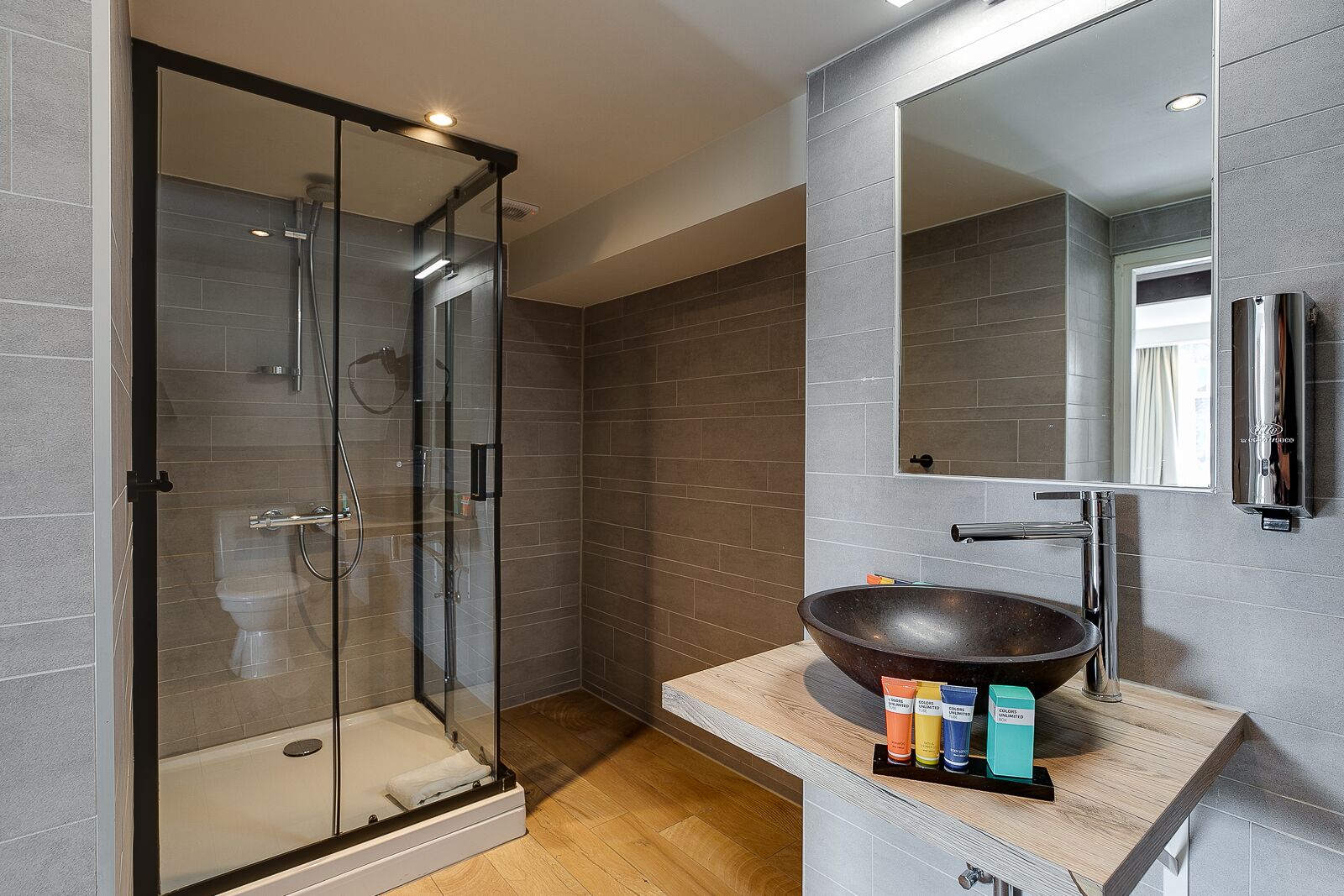A modern bathroom with a glass-enclosed shower, a large mirror, and a wooden vanity with a bowl sink.