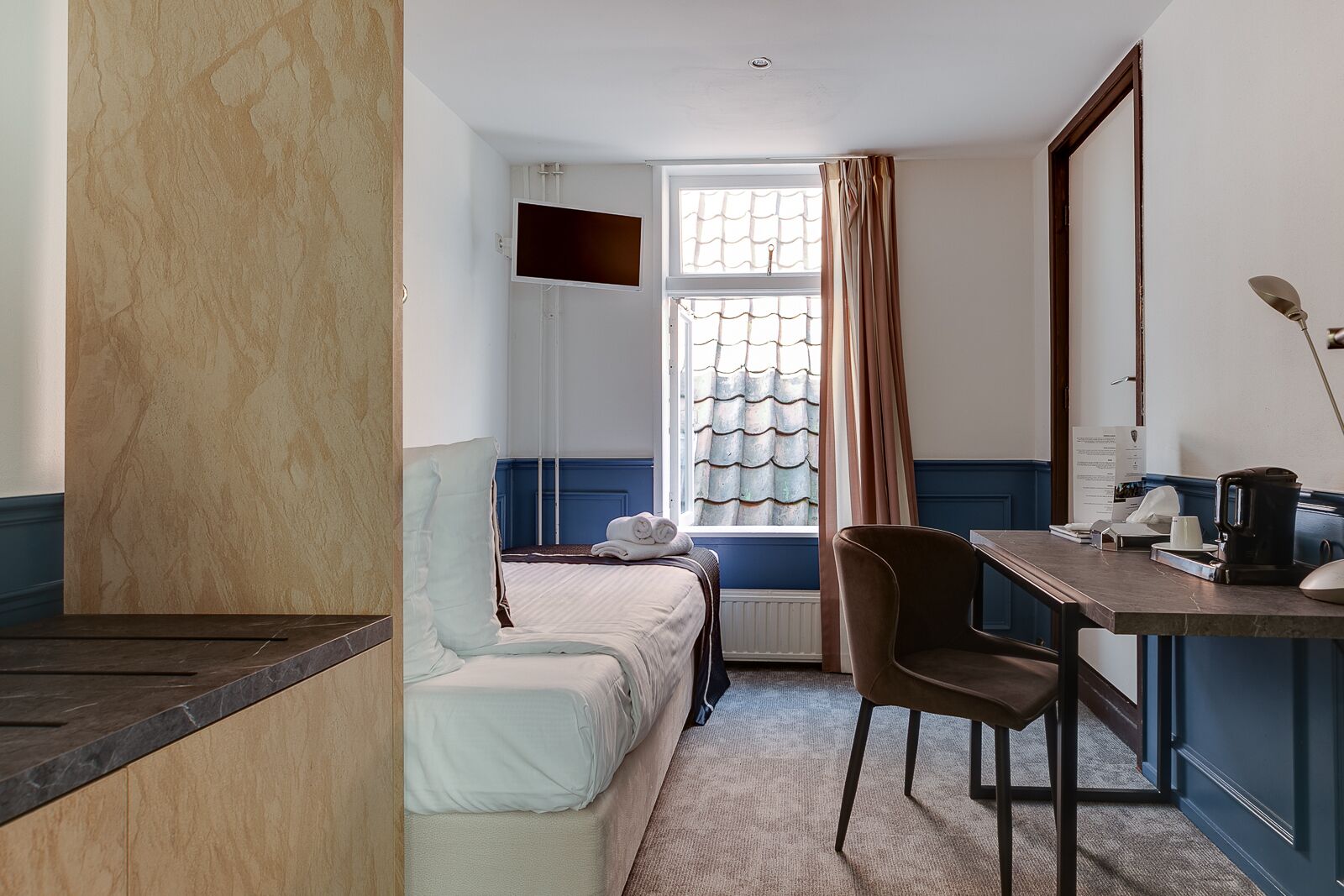 A hotel room with a bed, a desk, a chair, a TV, and a window with curtains.