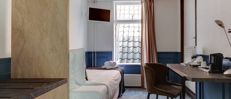 A hotel room with a bed, a desk, a chair, a TV, and a window with curtains.