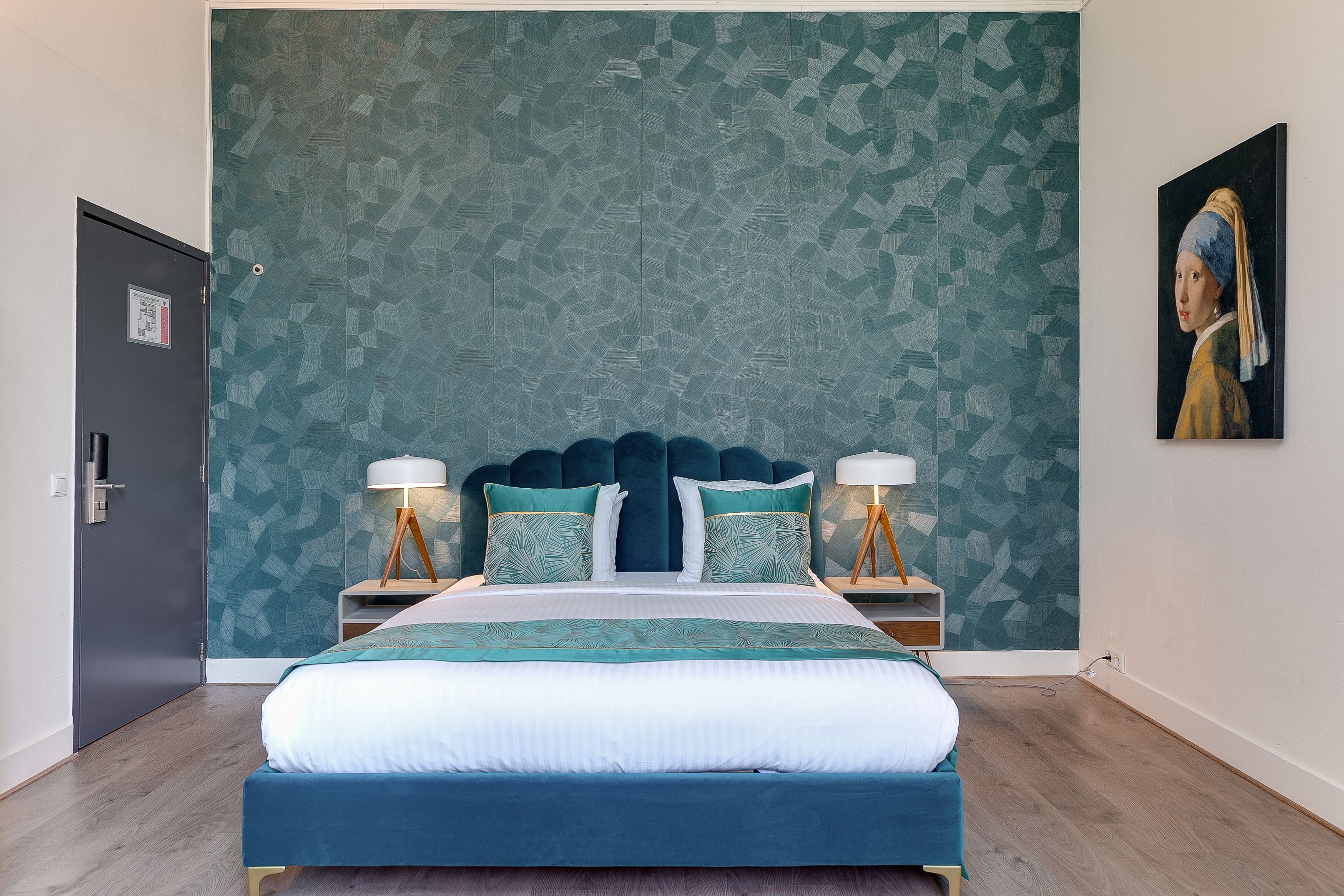 A neatly arranged hotel room with a large bed, two bedside tables with lamps, a patterned wall, and a painting on the wall.