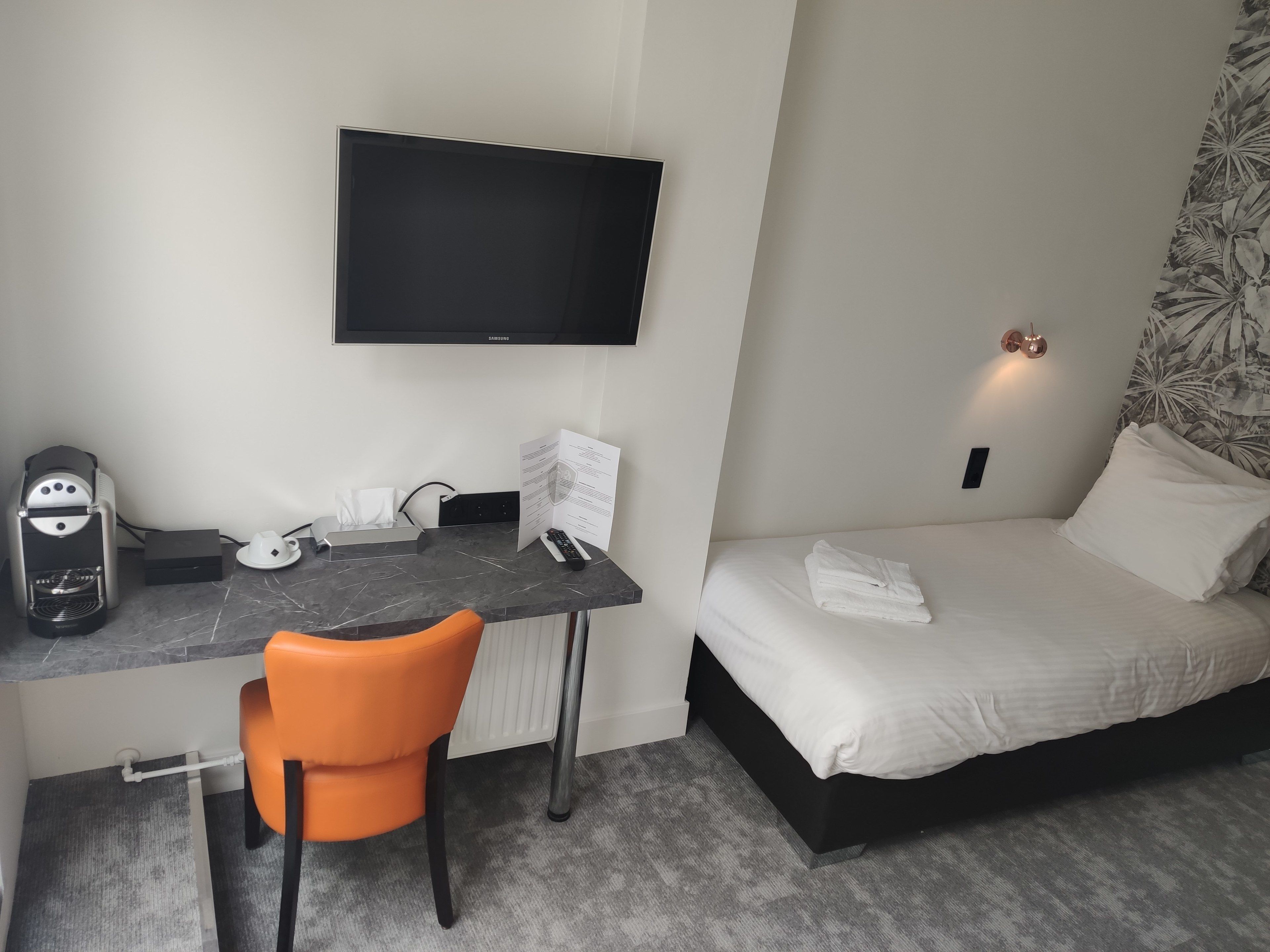 A hotel room with a bed, a desk with a chair, a television, and a coffee maker.
