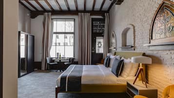 Habitación de hotel con cama, escritorio, silla, lámpara y ventana con cortinas.