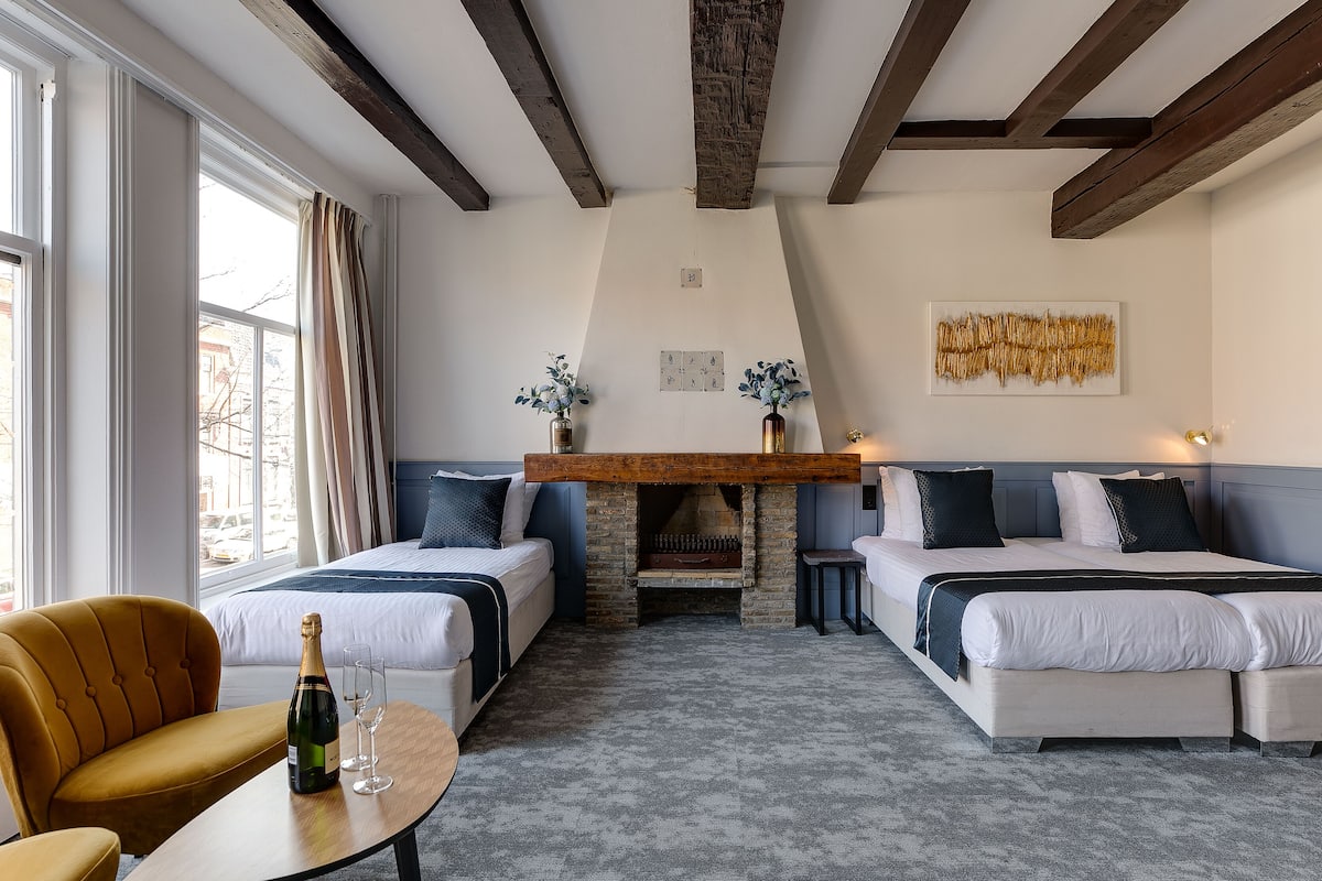 A hotel room with two beds, a wooden ceiling, a fireplace, and a view of the outside.
