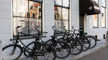 Diverse biciclette parcheggiate di fronte a un edificio con ampie finestre e un tendone nero.