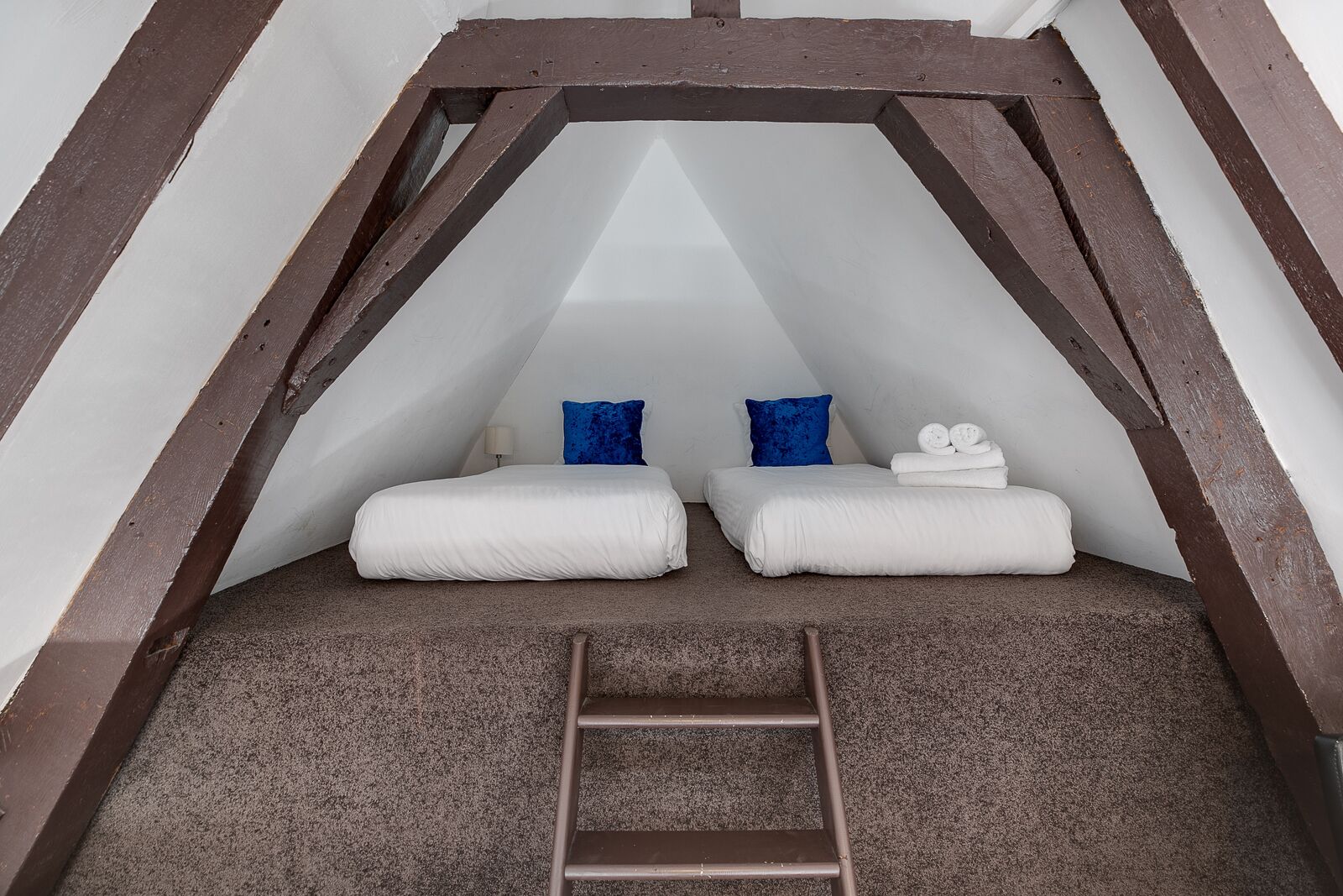 Ein kleines, dreieckiges Schlafzimmer im Dachgeschoss mit zwei Betten, einer Leiter und einer weißen Wand.
