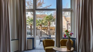 A room with large windows, two yellow chairs, a small table, and a vase with flowers. - Hotel Royal Bridges (Delft)