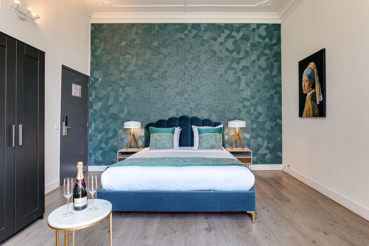 A hotel room with a large bed, a minibar, a door, and a wall with a geometric pattern.