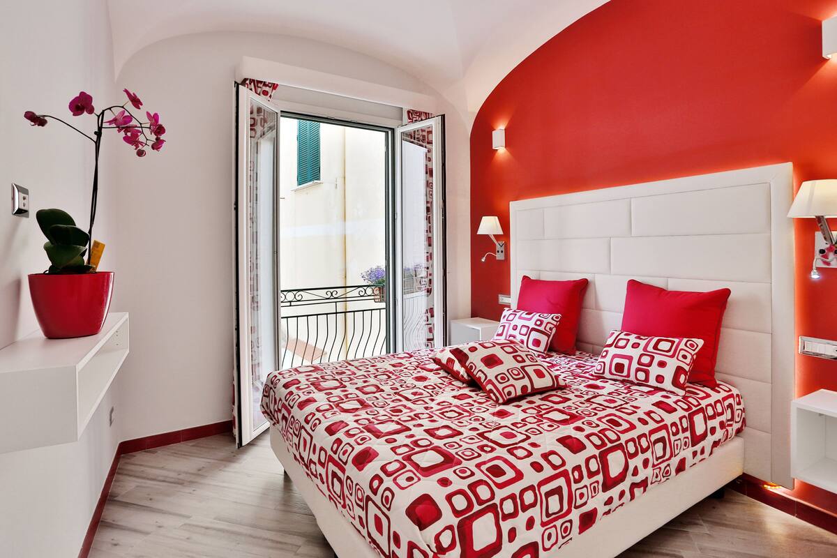 A bedroom with a red and white patterned bedspread, a potted orchid, and a white headboard.