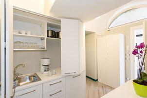 Una cocina compacta con lavamanos integrado, armarios blancos y cafetera.