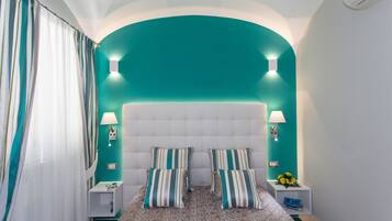 A bedroom with a teal accent wall, a tufted headboard, two bedside tables with lamps, and striped pillows.