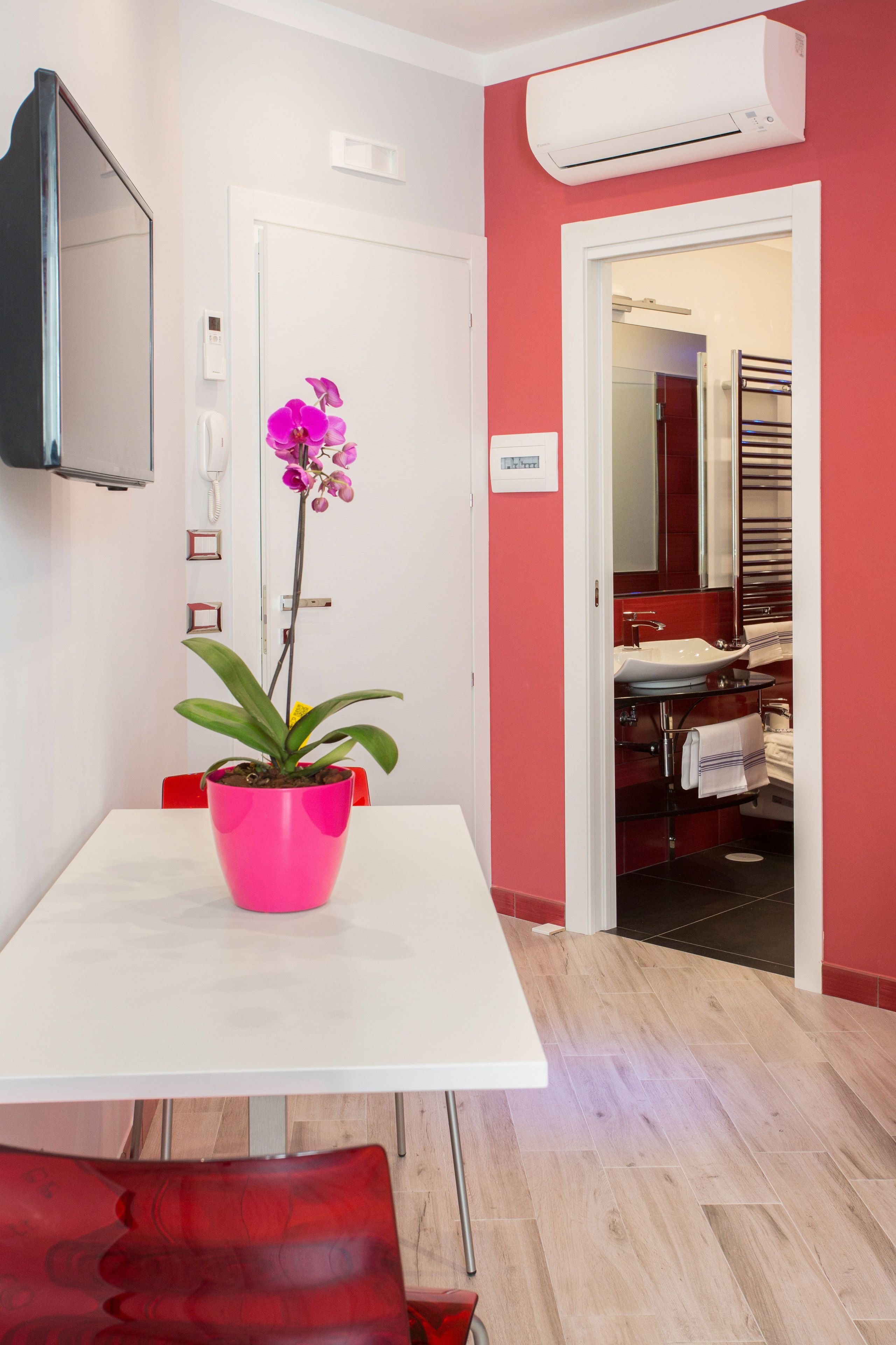 A modern bathroom with a white sink, a mirror, and a red wall.