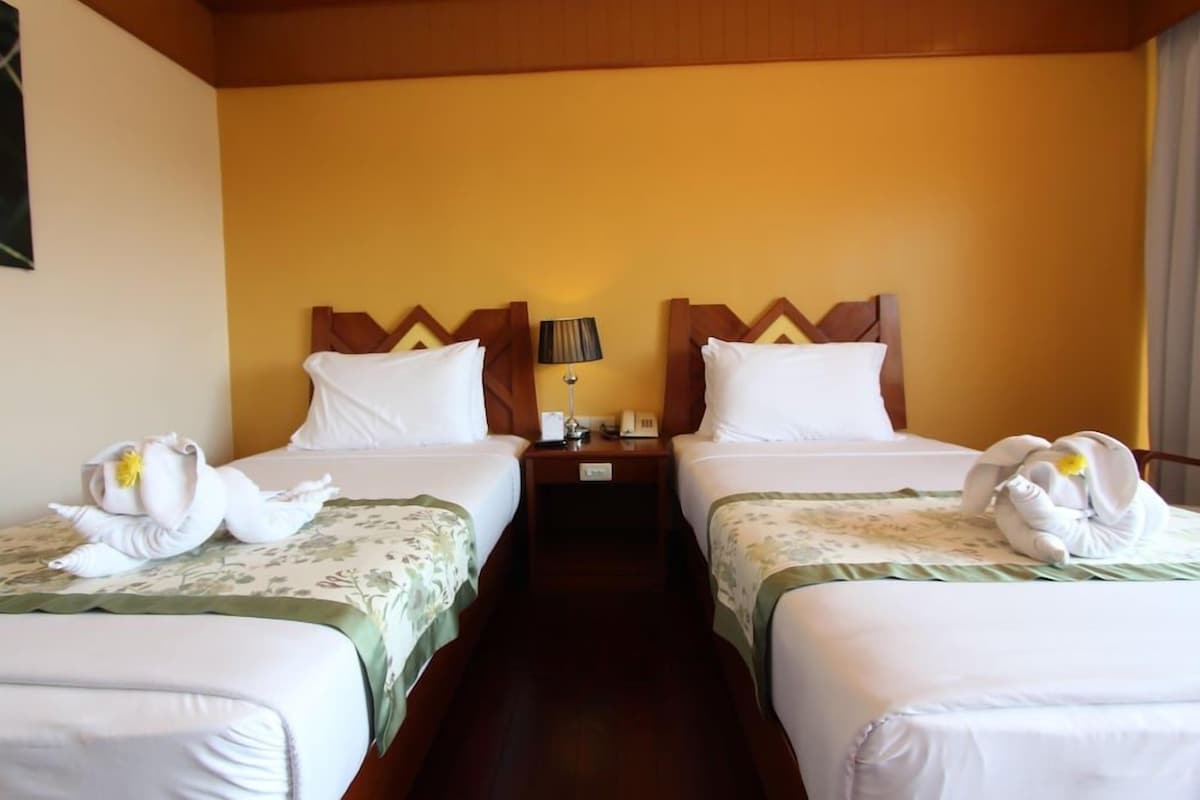 A hotel room with two beds, each with a wooden headboard, a nightstand between them, and a lamp.
