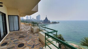 A balcony with a tiled floor, a railing, and a view of the sea and a distant cityscape. - Garden Sea View Resort (Pattaya)