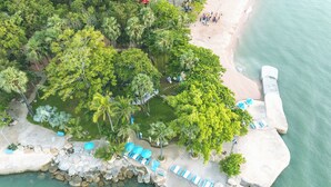 An aerial view of a beach resort with a rocky shoreline, palm trees, and a swimming area with lounge chairs. - Garden Sea View Resort (Pattaya)