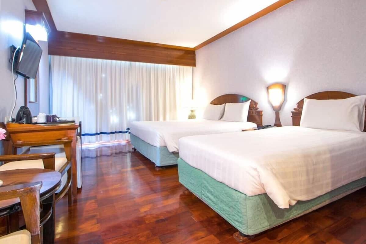 A hotel room with two beds, a desk, a chair, a television, and a window with curtains.