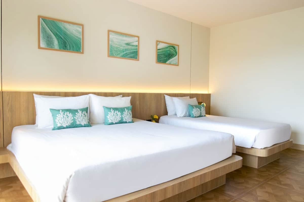 A hotel room with two beds, a wooden headboard, and three abstract paintings on the wall.