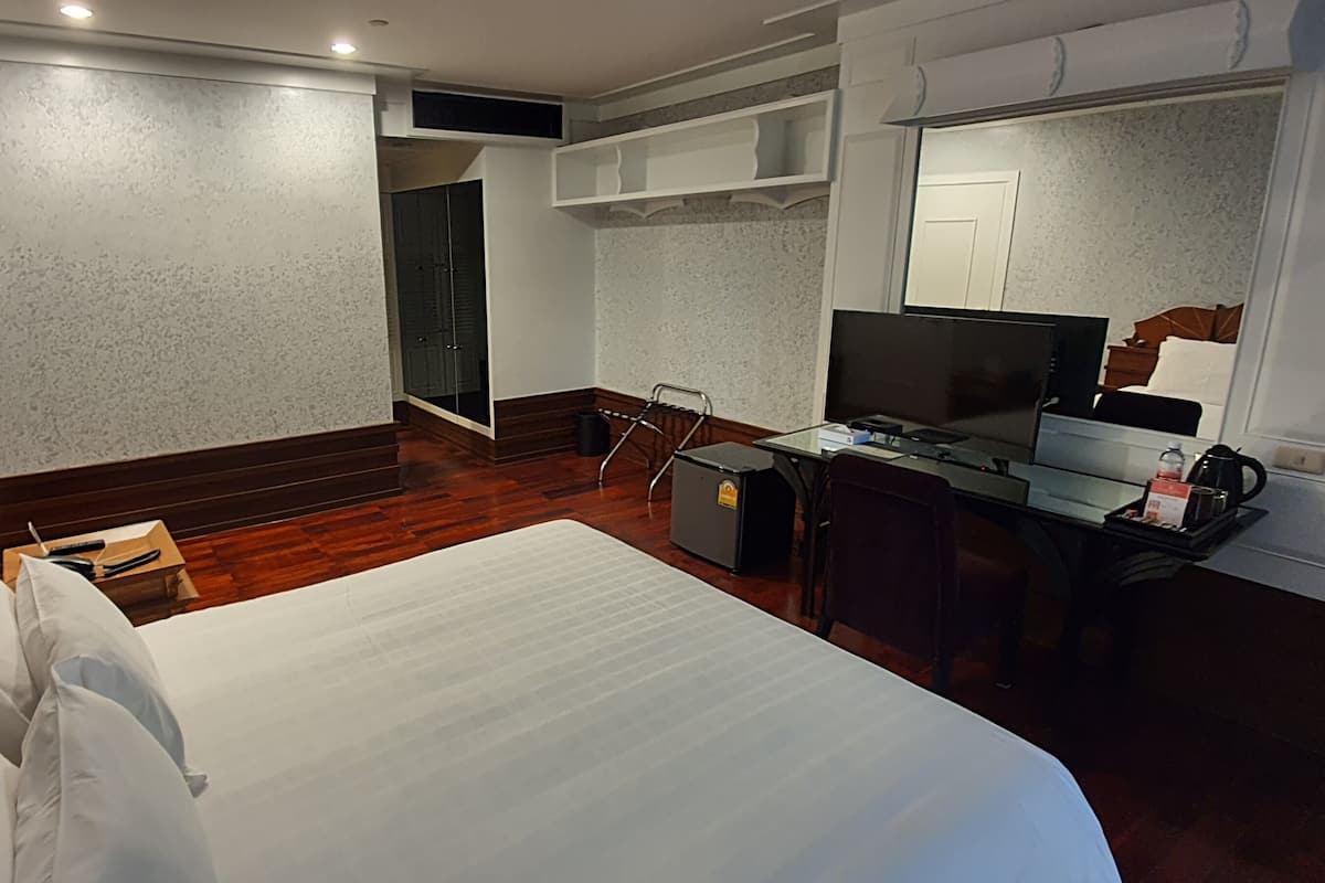 A hotel room with a large bed, a desk with a computer, a TV, and a small seating area.