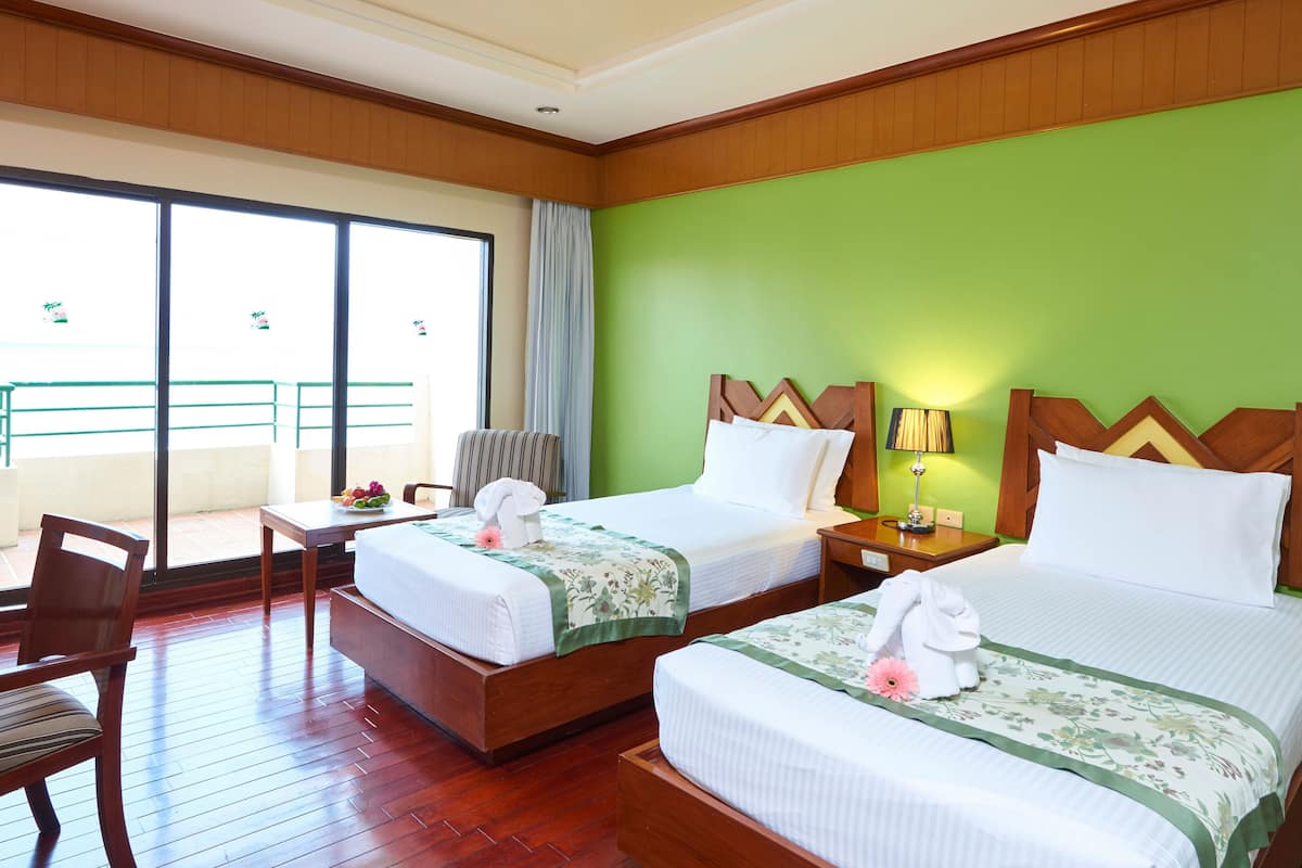 A hotel room with two beds, a chair, a small table with fruit, and a balcony with a railing.