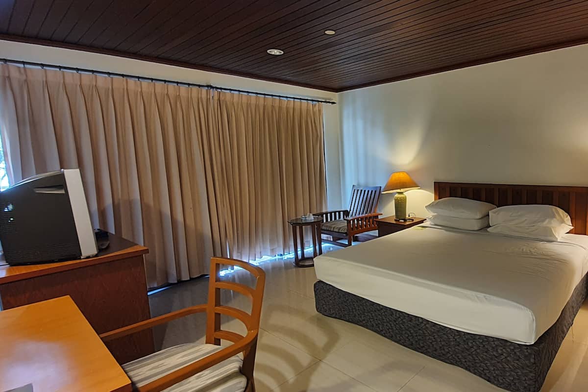 A hotel room with a bed, two bedside tables with lamps, a desk with a laptop, a chair, and a large window with curtains.