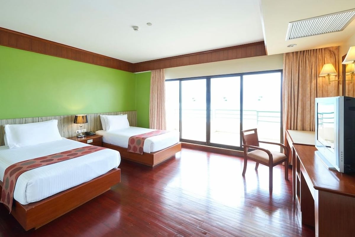 A hotel room with two beds, a desk, a chair, and a television.