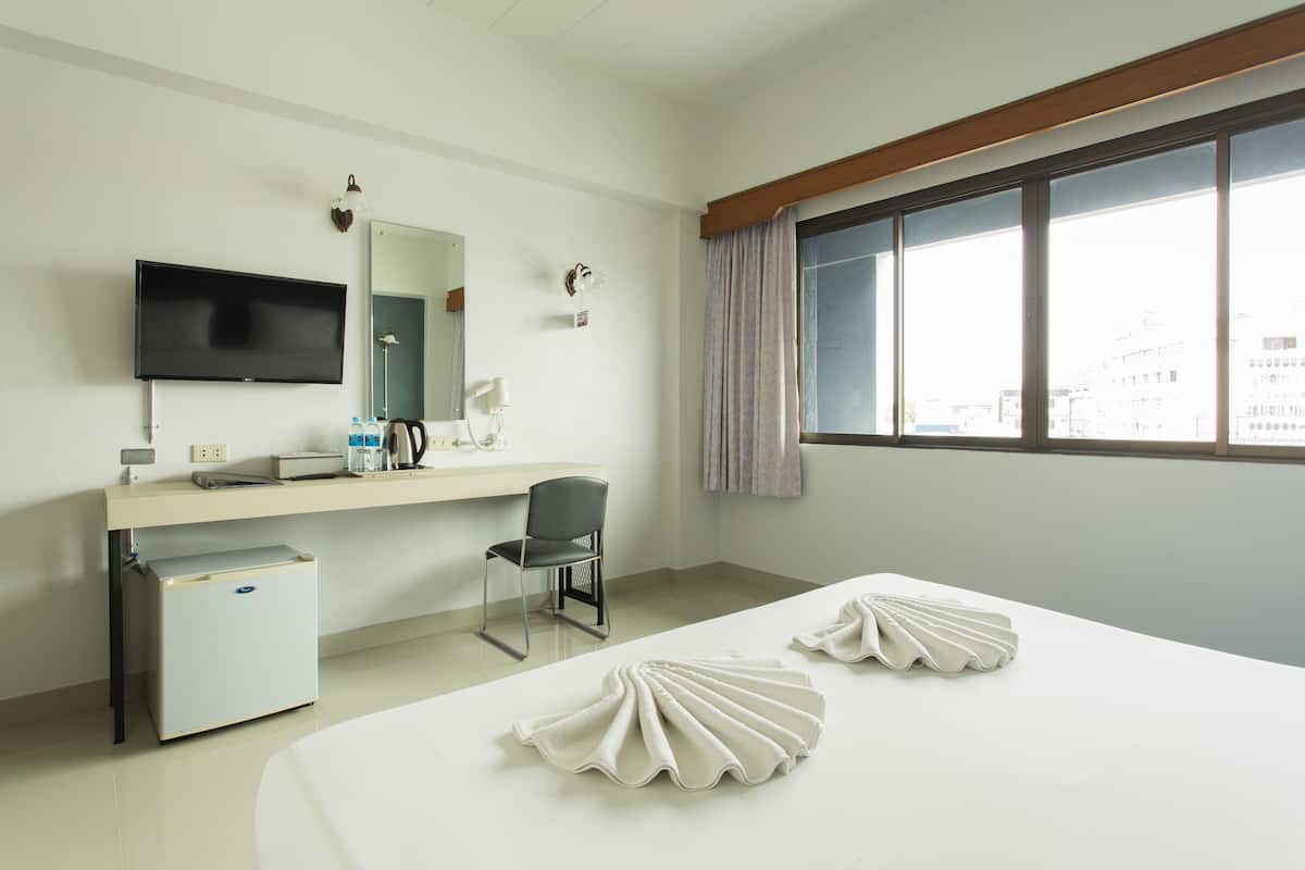 A hotel room with a bed, a desk, a chair, a TV, a mini-fridge, and a window with curtains.