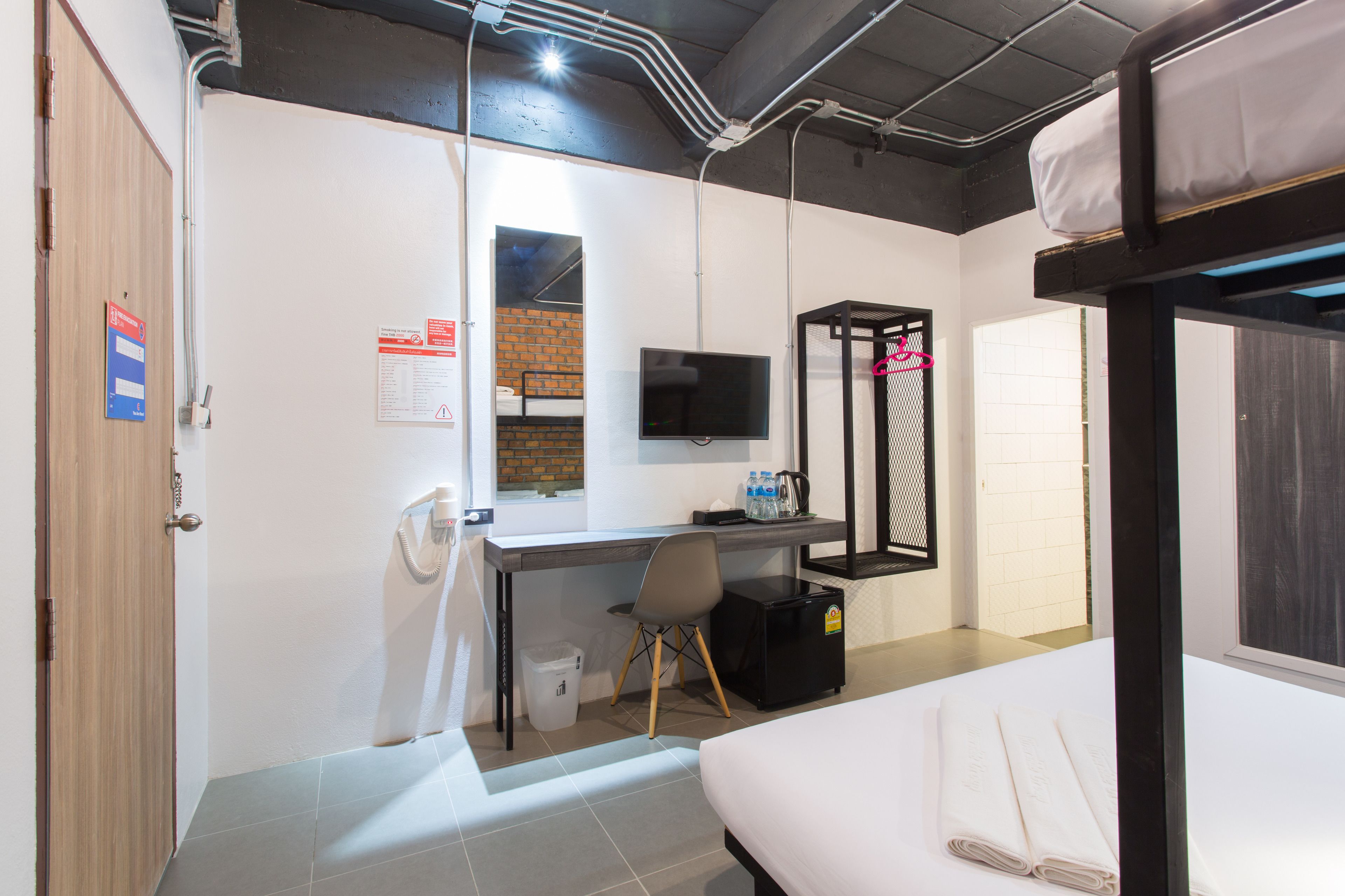 A dormitory room with a bed, desk, chair, TV, and a small refrigerator.