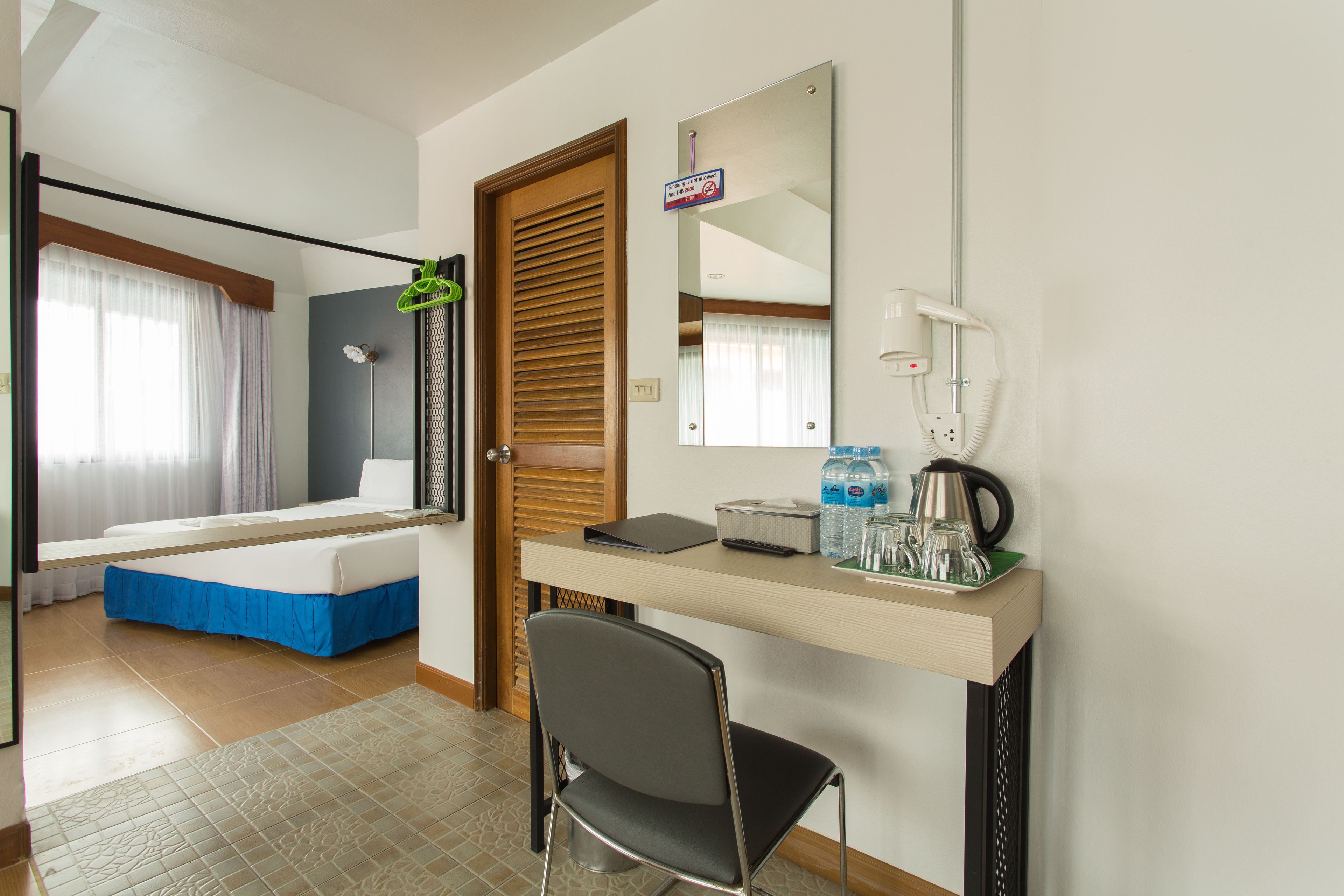 A hotel room with a bed, a desk with a chair, a mirror, and a small table with toiletries.
