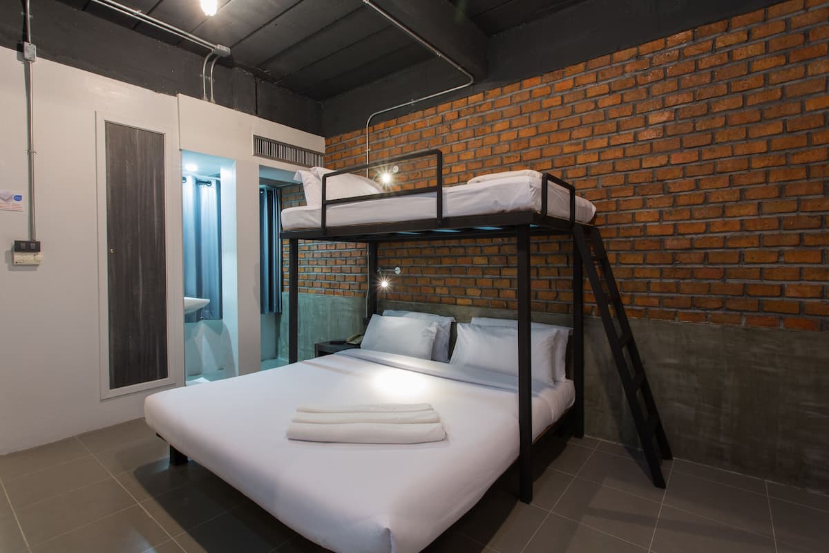 A bunk bed room with a brick wall, a window, and a bathroom visible through a glass door.