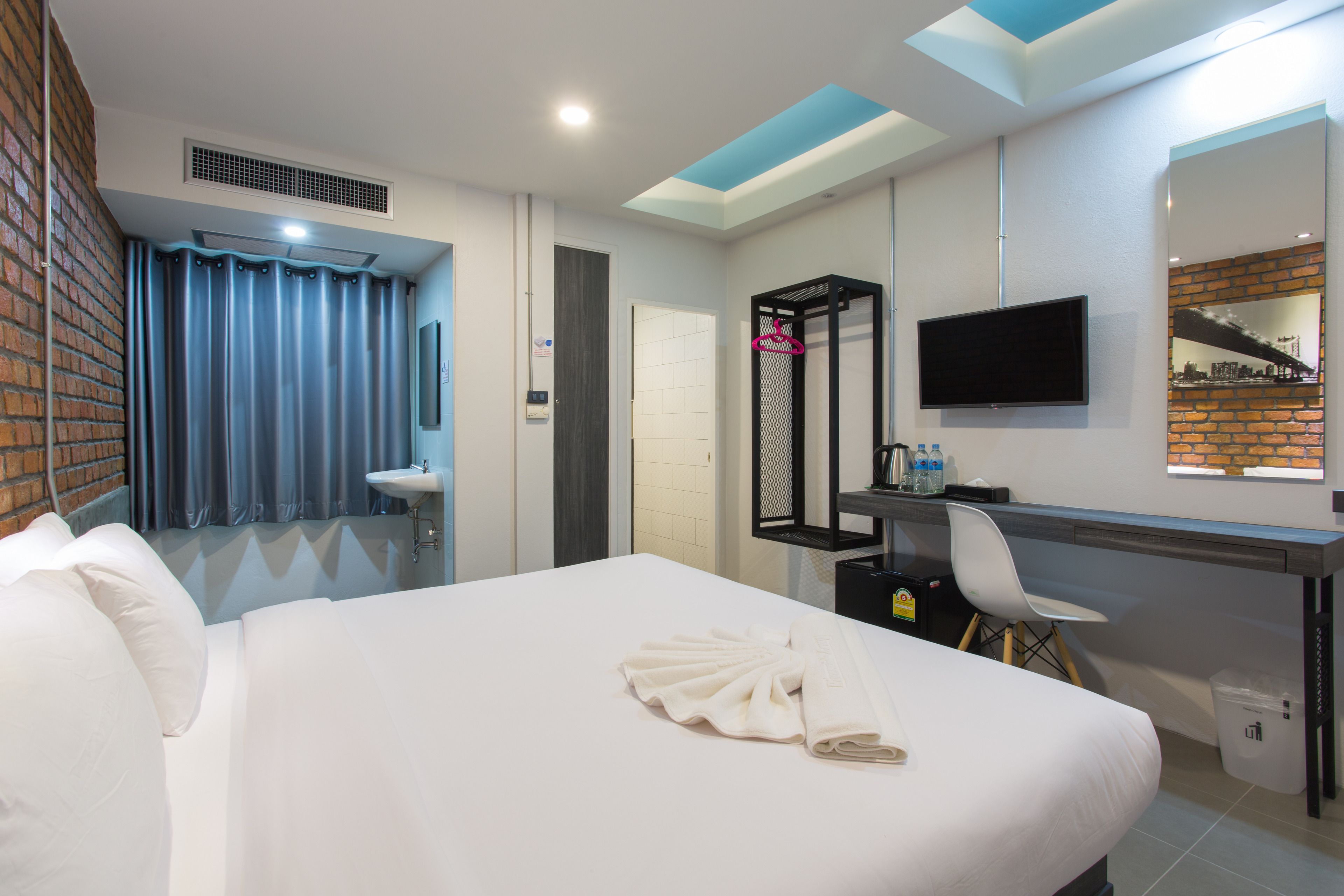 A hotel room with a large bed, a desk with a chair, a TV, and a bathroom with a sink and shower.