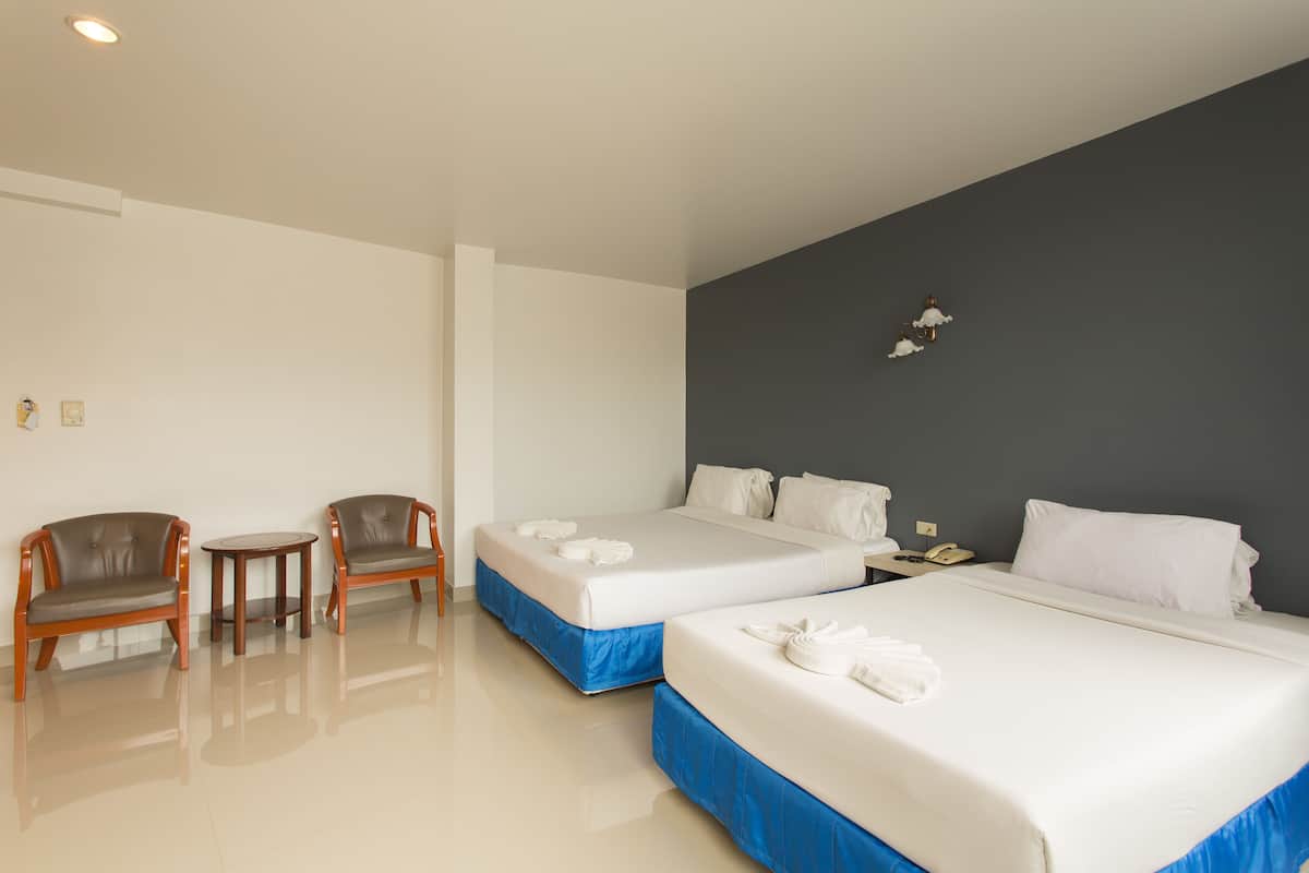 A hotel room with two beds, a small table, two chairs, a nightstand, and a wall-mounted lamp.