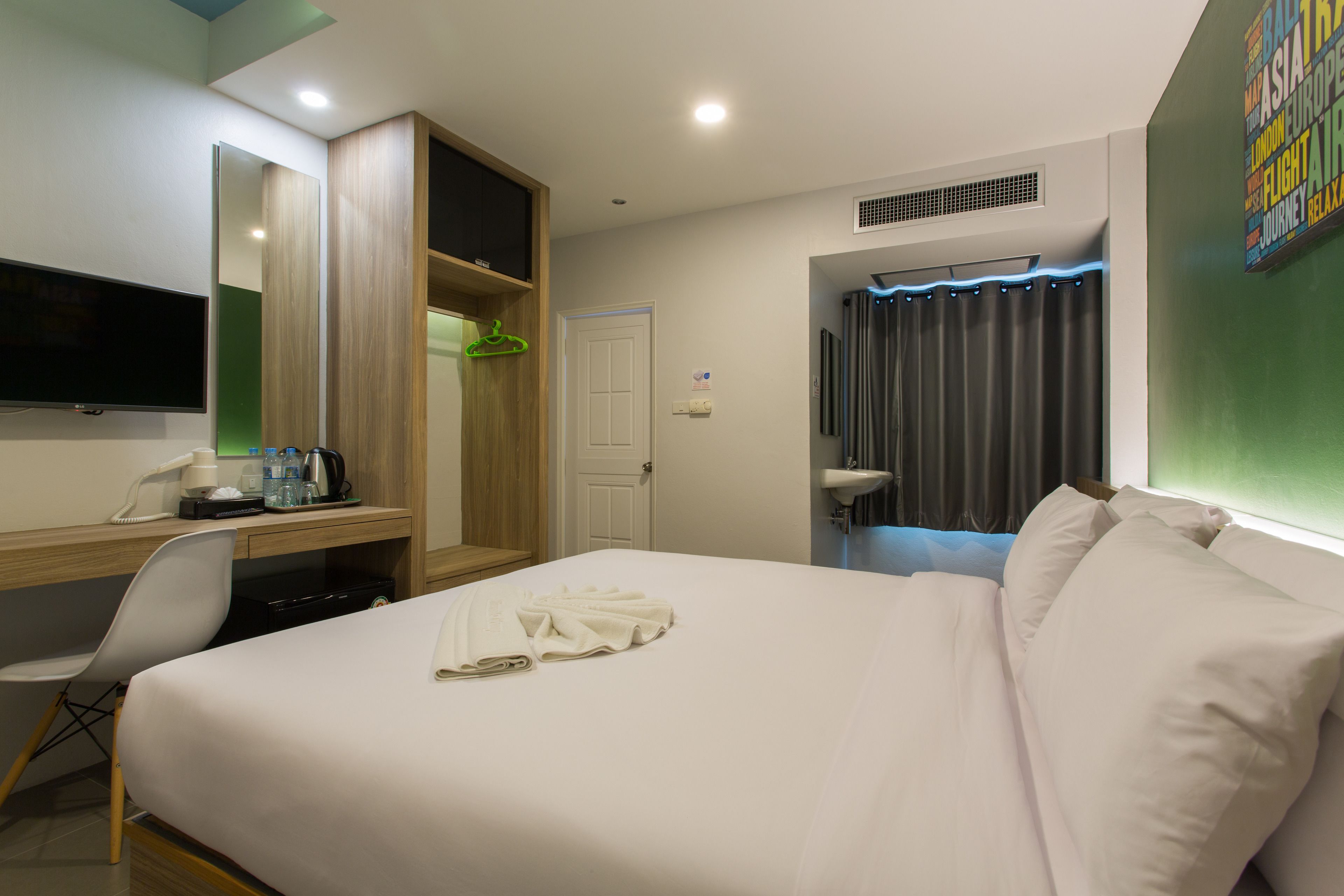 A hotel room with a bed, a desk with a chair, a TV, a wardrobe, a bathroom with a sink, and a shower curtain.