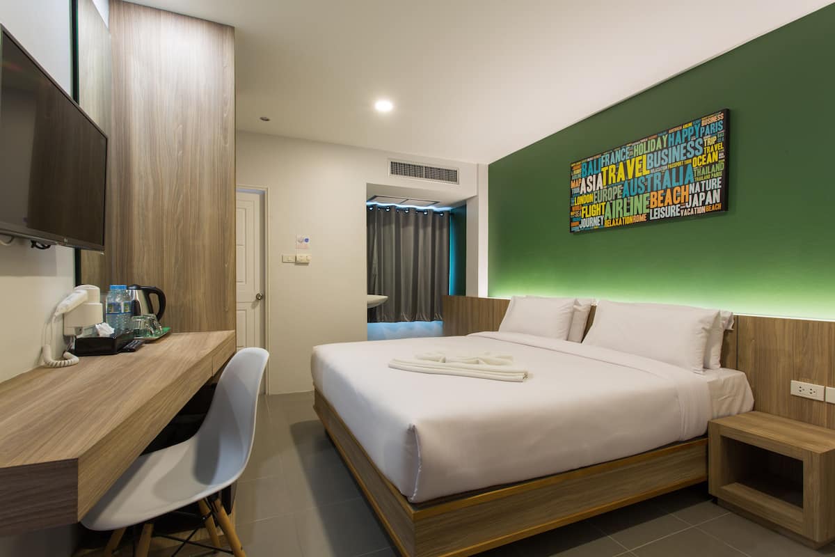 A hotel room with a bed, a desk, a chair, a TV, and a wall art piece.