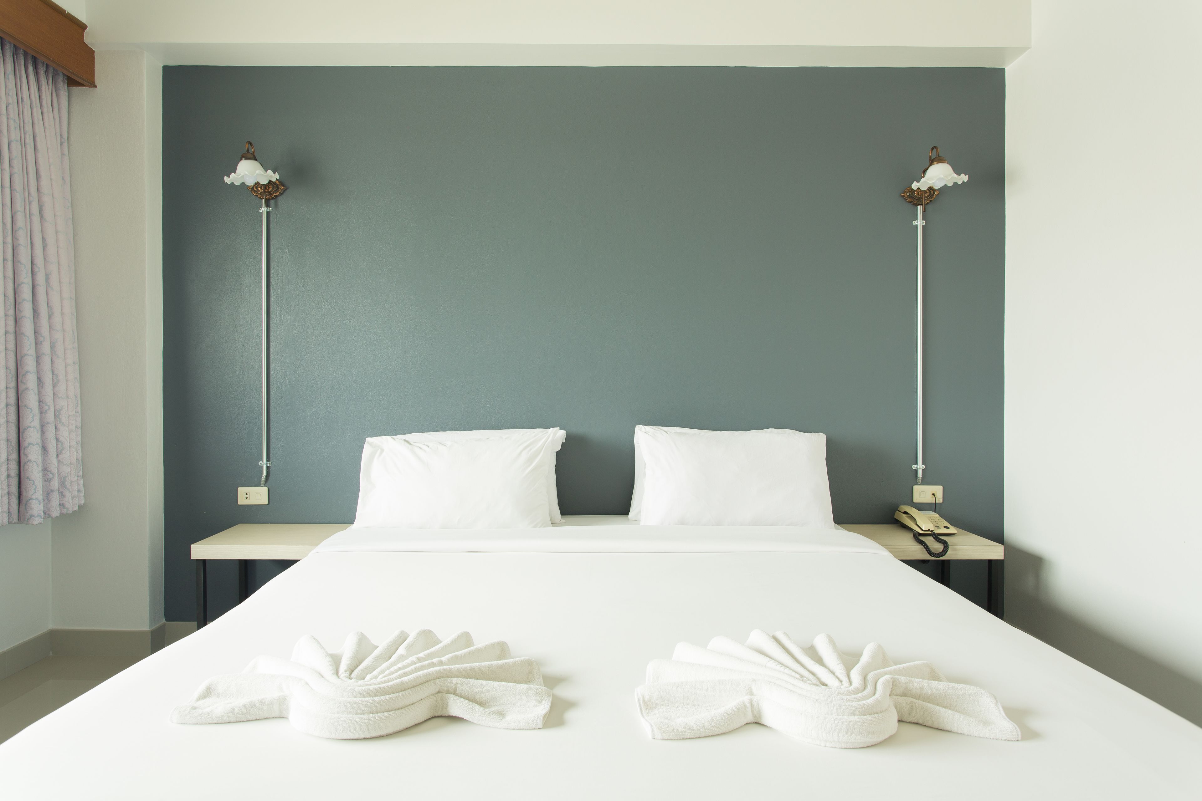 A hotel room with a bed, two pillows, a bedside table with a phone, and two towels on the bed.