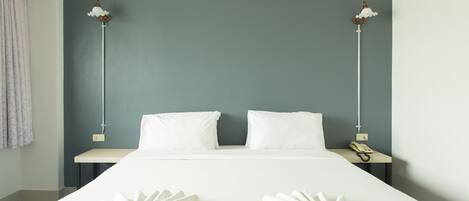 A hotel room with a bed, two pillows, a bedside table with a phone, and two towels on the bed.