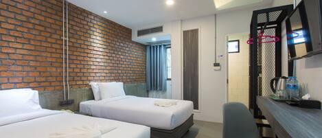 A hotel room with two beds, a desk, a chair, a TV, and a brick wall.