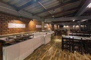 Zona de desayuno tipo buffet con estaciones de servicio de acero inoxidable, pared de ladrillo y mesas y sillas de madera.
