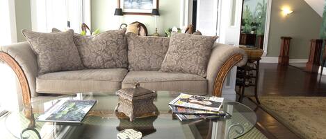 A living room with a sectional sofa, a glass coffee table, and a view of the outdoors through a window.