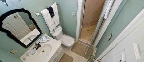 Une salle de bain avec un lavabo blanc, un miroir, des toilettes et une douche.
