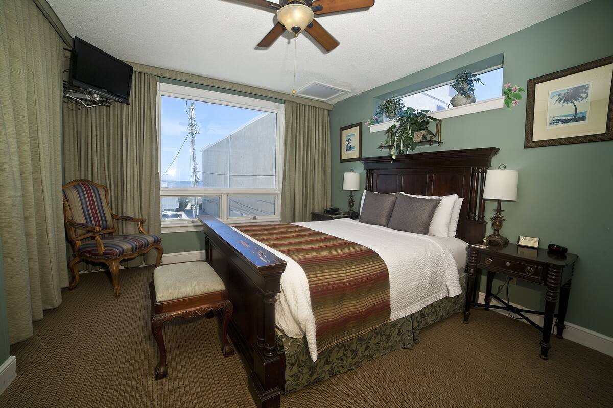 A hotel room with a bed, a chair, a desk, a television, and a window with curtains.